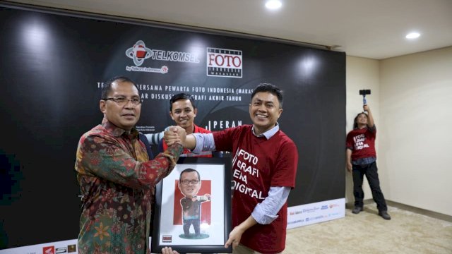 Ketua Pewarta Foto Indonesia (PFI) Makassar, Ocha Alim Bahri menyerahkan cenderamata kepada Wali Kota Makassar, Moh. Ramdhan Pomanto, usai diskusi akhir tahun yang diselenggarakan di Gedung Miring Telkomsel, Jl. AP. Pettarani Makassar, Sabtu (29/12/2018).