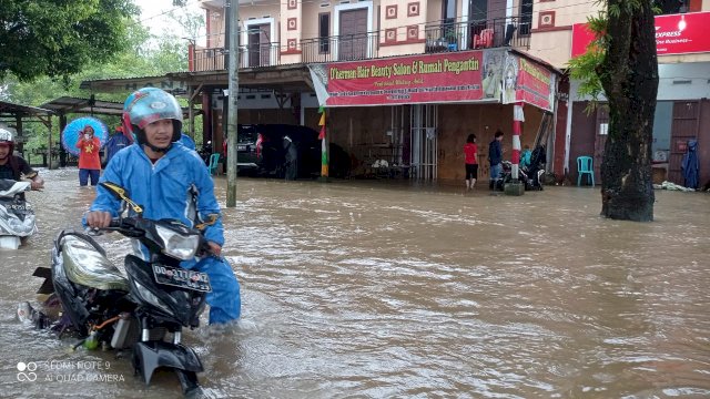 Pengendara roda dua terpaksa turun dan mendorong kendaraannya karena mogok akibat banjir sepanjang 100 meter di jalan poros Kelurahan Bontomanai - Desa Pakkatto, Kecamatan Bontomarannu, Rabu (10/03/2021). (Rhany)