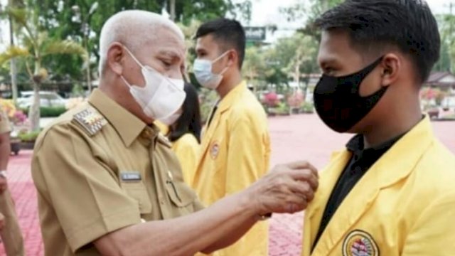 Bupati Asahan, Surya, memakaikan PIN tanda kelulusan Mahasiswa UNA, Senin (22/03/2021).