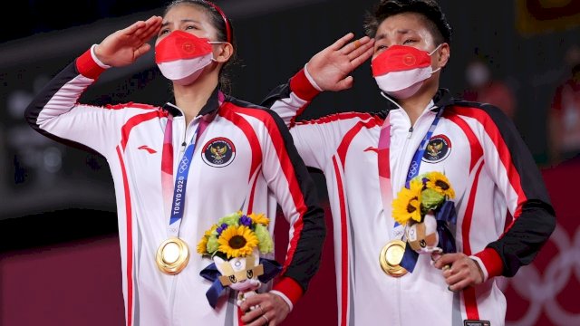 Greysia Polii (kiri) dan Apriyani Rahayu (kanan) saat memberi penghormatan kepada bendera Merah Putih dalam acara penyerahan medali Olimpiade Tokyo 2020. Foto: NOC Indonesia