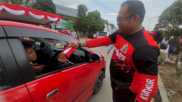 Wakil Bupati Kutai Timur Kasmidi Bulang, memberikan bendera kepada salah seorang warga yang melintas, Jumat (11/8/2023). (Istimewa)